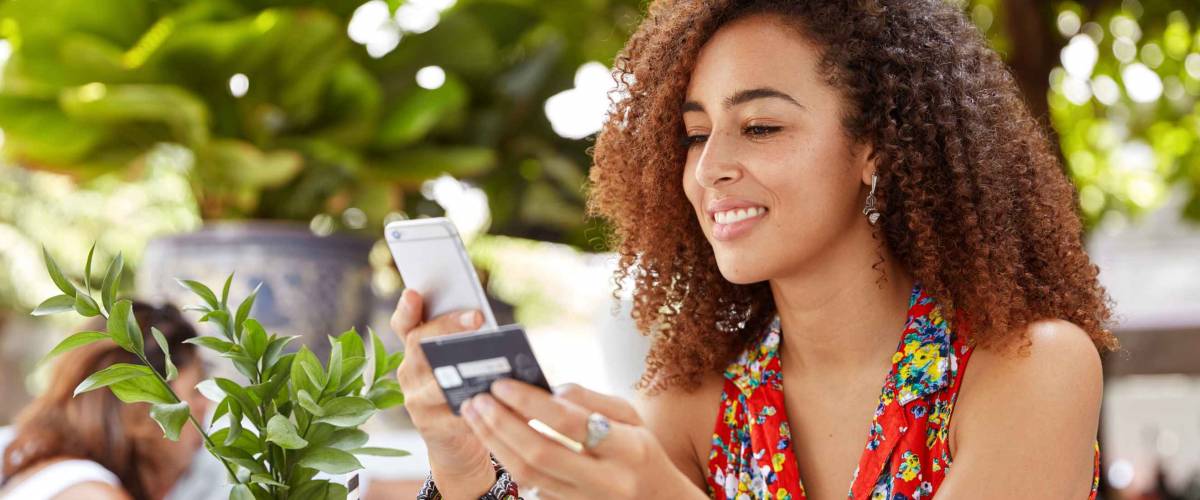 Shot of beautiful glad young female types number of credit card on smart phone