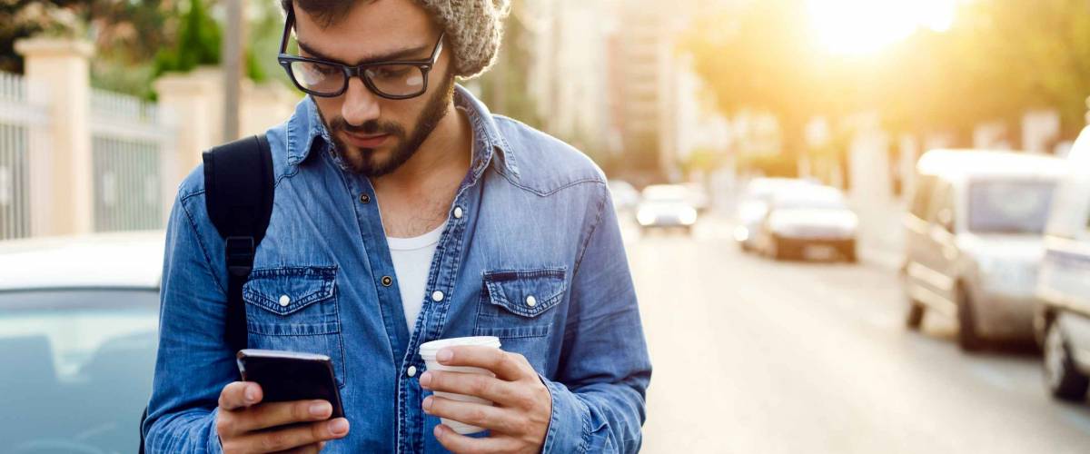Outdoor portrait of modern young man with mobile phone in the street.