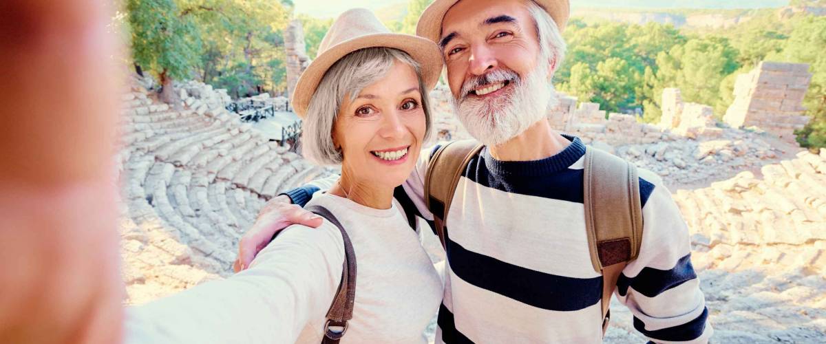 Tourism and technology. Traveling senior couple taking selfie together against ancient sightseeing background.