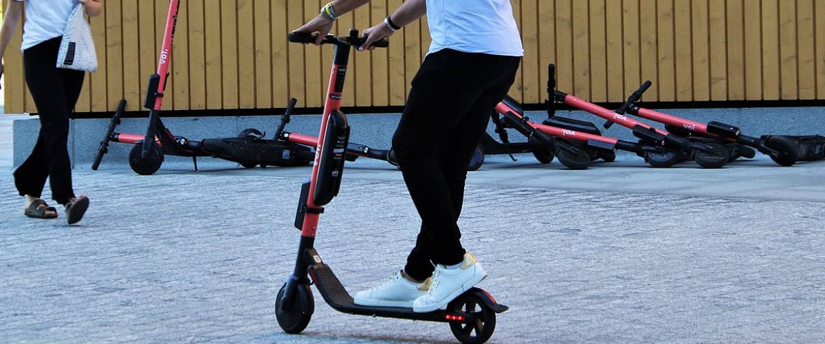 Man riding an electric scooter. In the background several other scooters lie on the ground