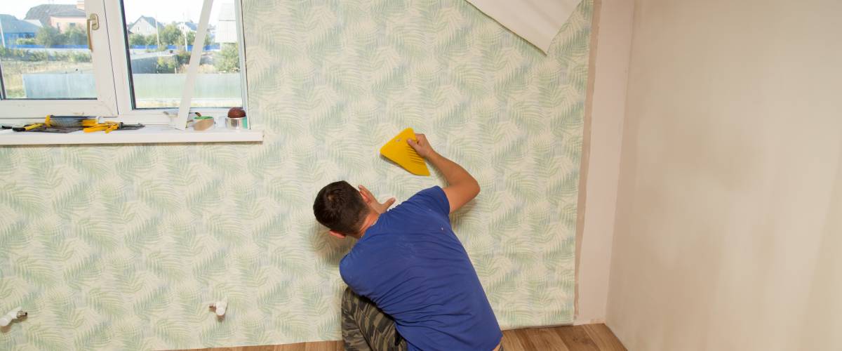 Man gluing wallpaper to walls of room