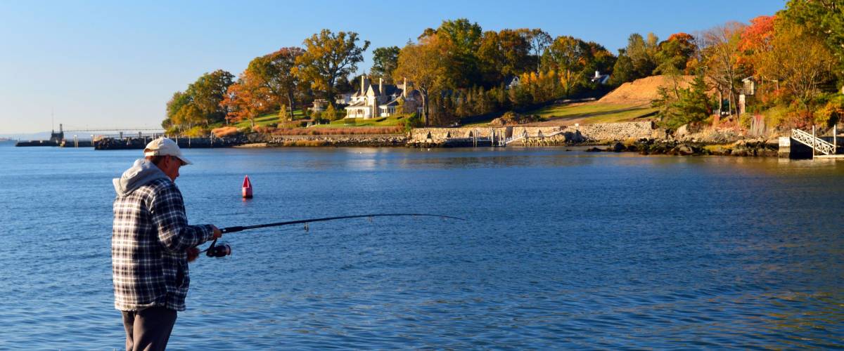 Greenwich, CT, USA October 27, 2013 An adult man casts his line to fish along the Greenwich, Connecticut waterfront in fall