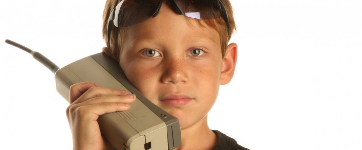 a young boy talks on a old 1980s era Brick Cell phone isolated on white