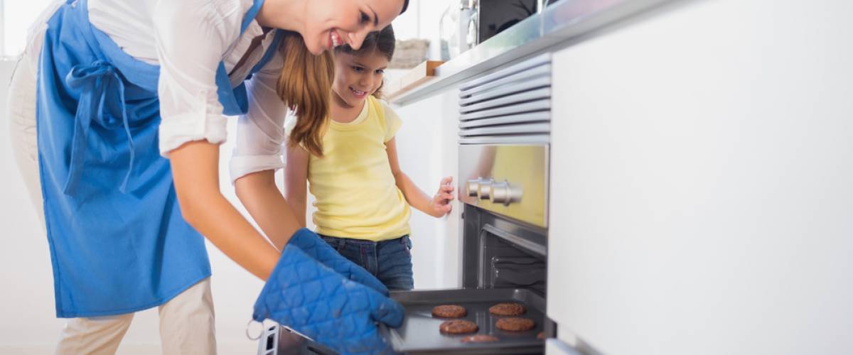 woman using oven mitts to take hot pan out of stove