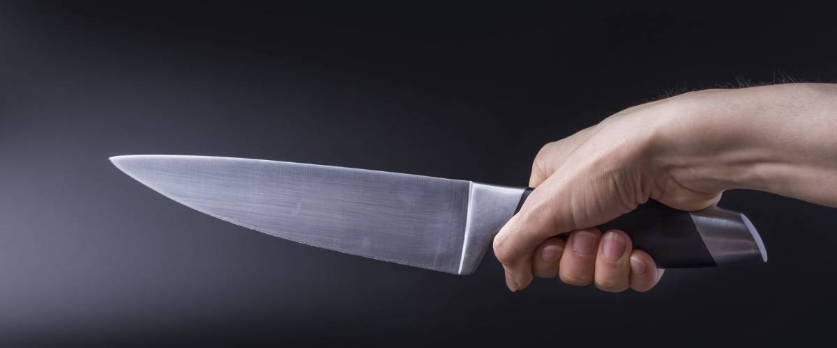 The concept of hand holding a large knife blade upwards diagonally on black background.