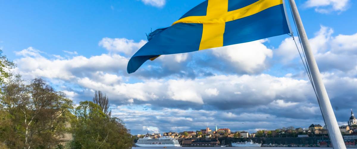 Swedish flag against blue sky with white clouds.