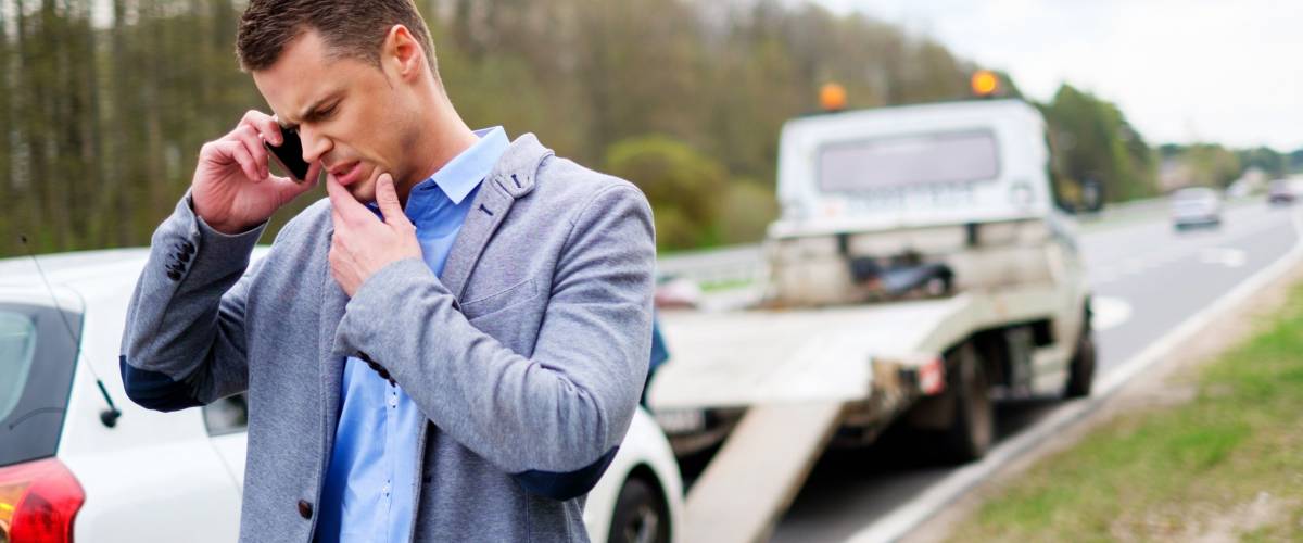 Man calling while tow truck picking up his broken car.