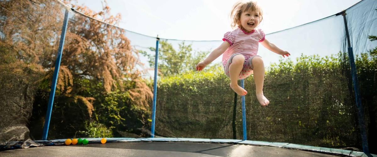 Little child enjoys jumping on trampoline - outside in backyard