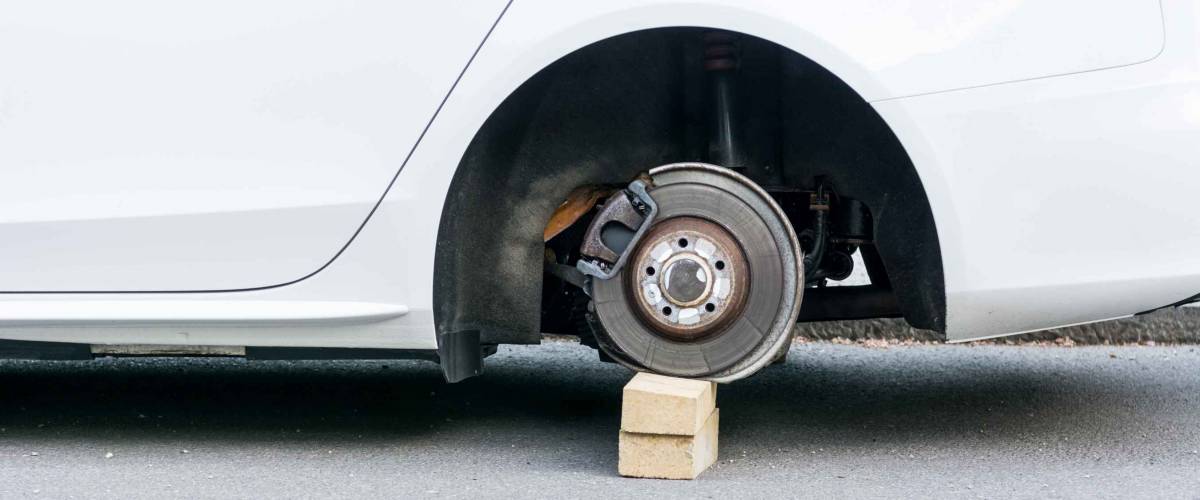 Car with stolen wheels. White vehicle left on wooden bricks.