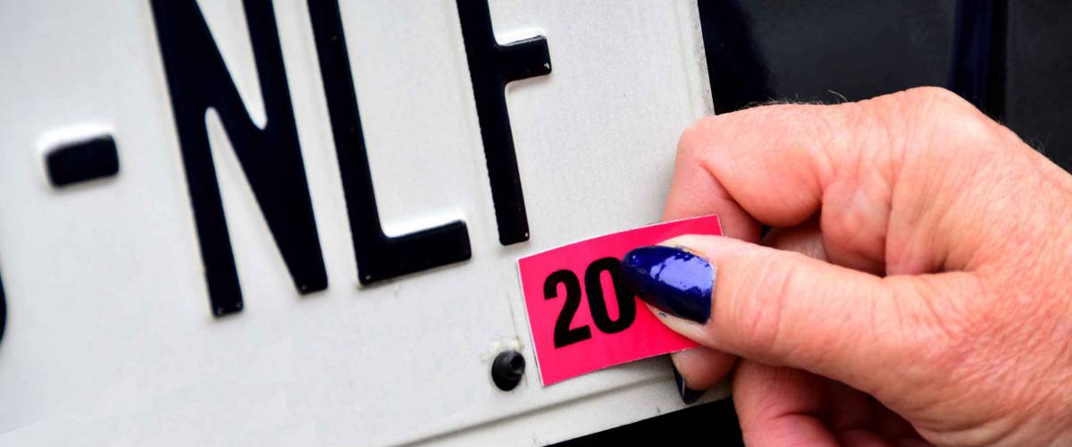 Female hands applying license plate registration annual sticker on white plate with black letters.