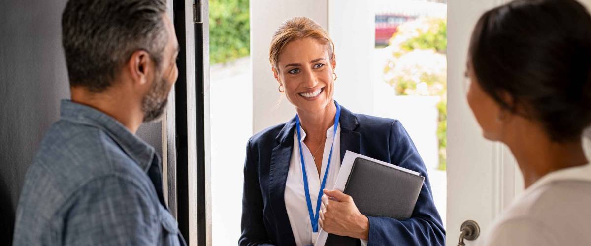 Couple opening the front door to smiling woman with paperwork