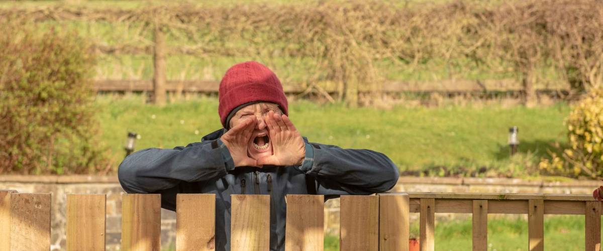 Senior woman shouting over a wooden gate outdoors in winter