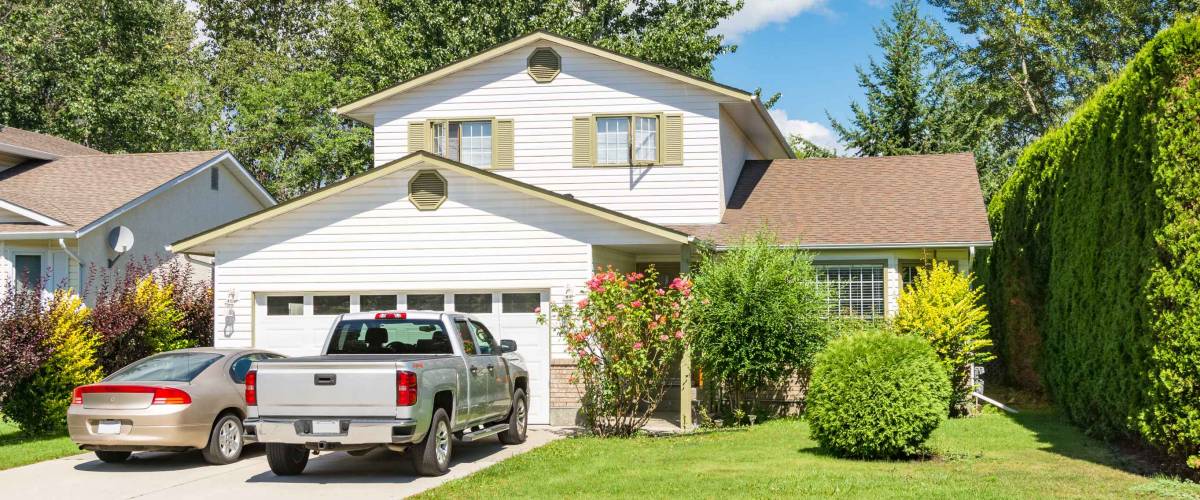 Main entrance of big residential house with car and truck parked on concrete driveway in front