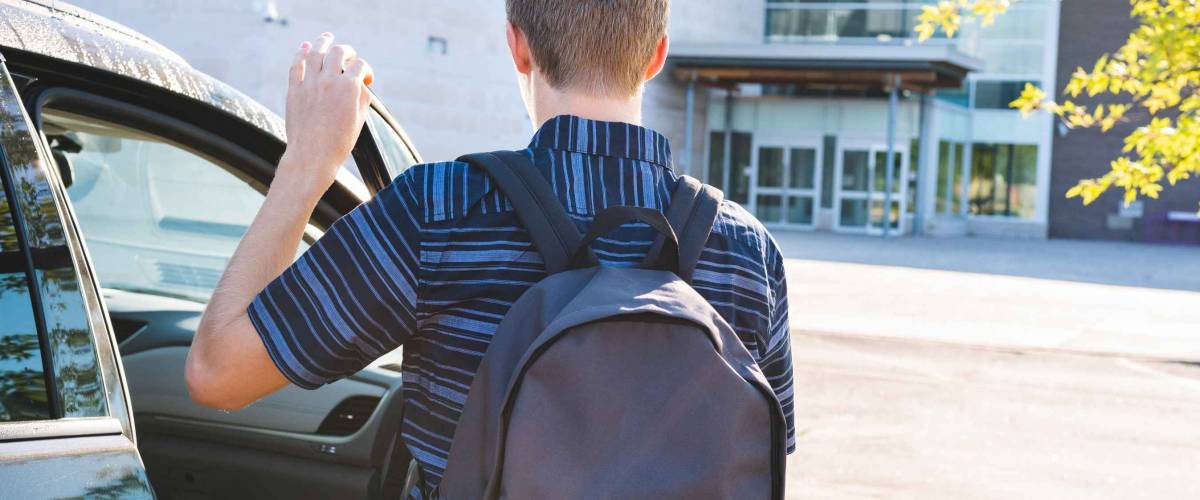 Teenager closing the door of his car that is parked in a school parking lot.