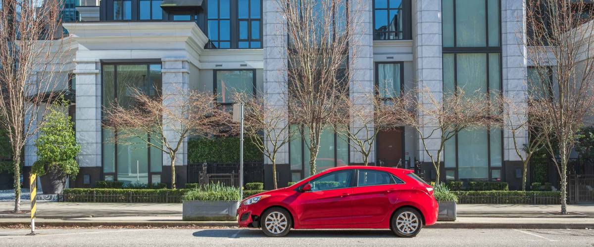 Red car on the empty urban street in a sunny day. Car parked in downtown of Vancouver Canada. Modern architecture view with car parked on a street. Nobody, street photo