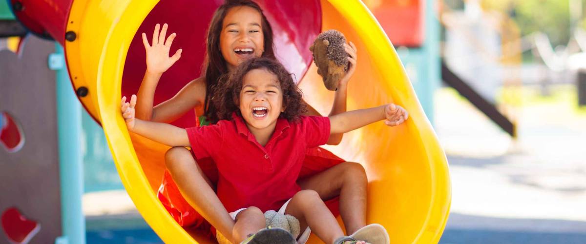 Kids on playground. Children play outdoor on school yard slide. Healthy activity. Summer vacation fun. Child playing in sunny park. Kid having fun on colorful slide.