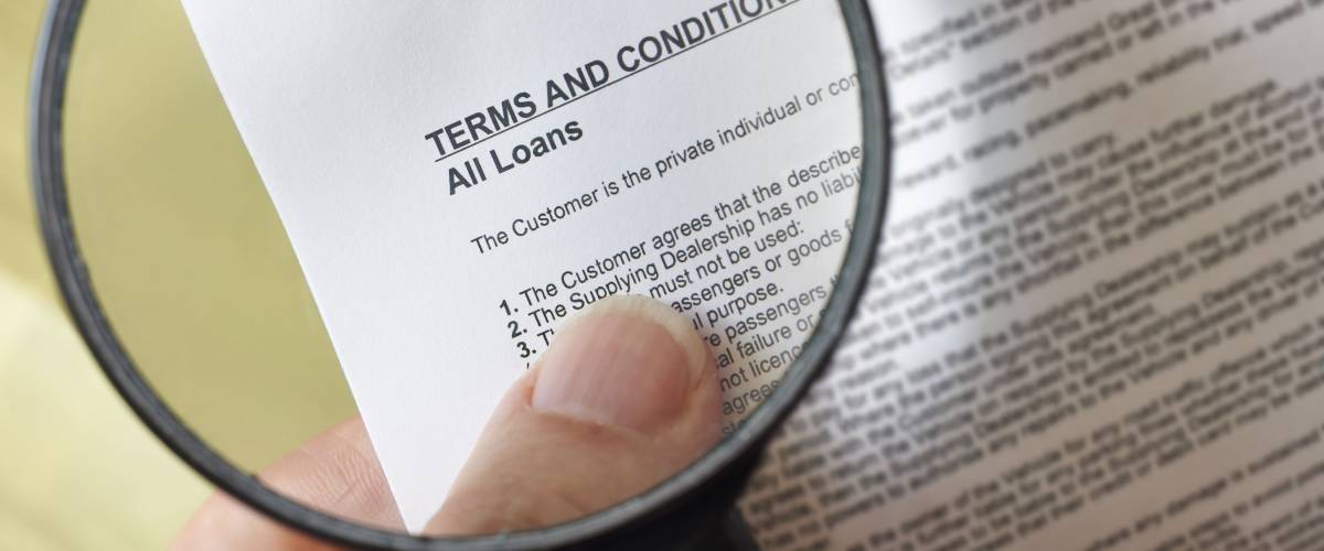 hands holding magnifying glass reading terms and conditions of loan agreement