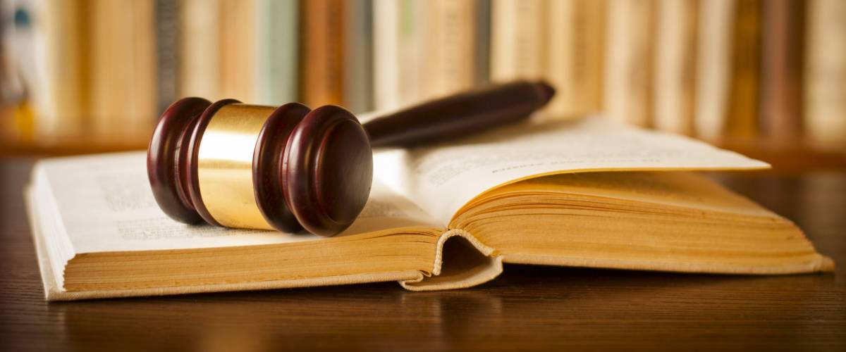 Open law book with a judges gavel resting on top of the pages in a courtroom or law enforcement office