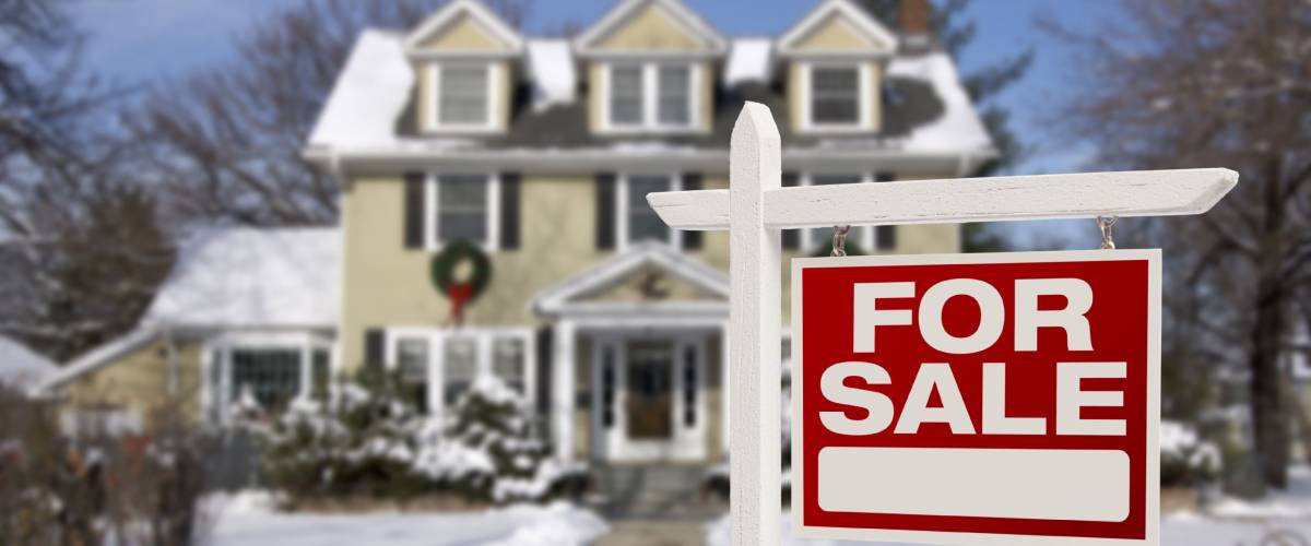 Home For Sale Real Estate Sign in Front of Beautiful New House in the Snow.