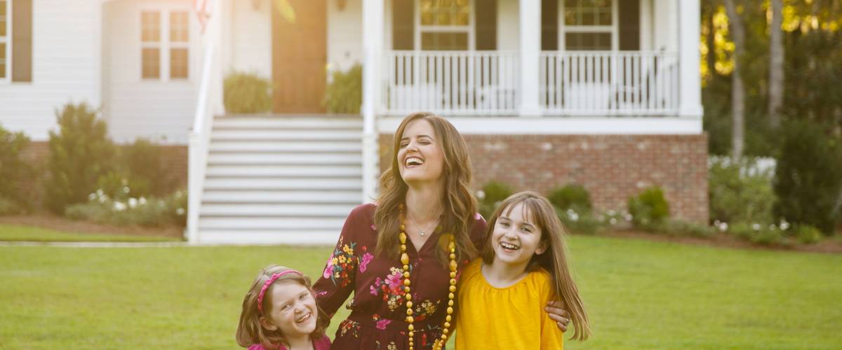 Mom and Two Daughters Laughing and Hugging Outside their New Farmhouse Home