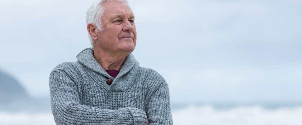 Smiling senior man standing with arms crossed on the beach