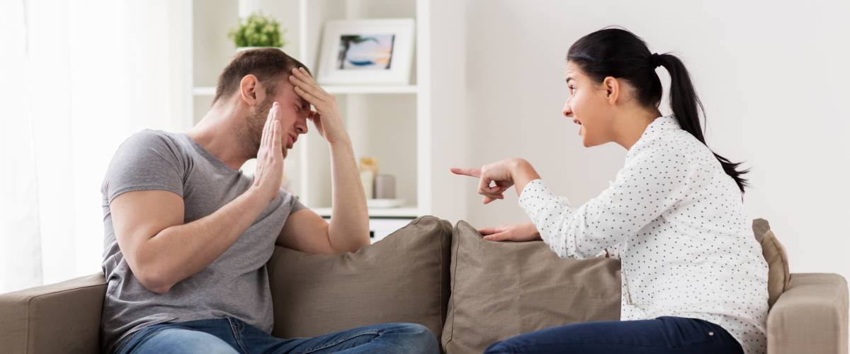 Woman madly pointing at man on couch