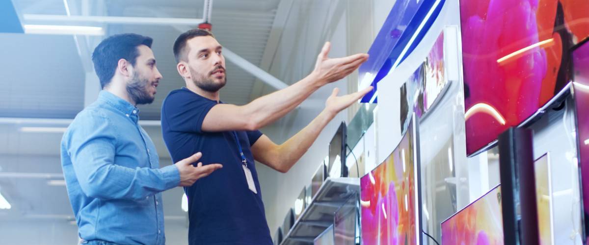 In the Electronics Store Professional Consultant Shows TV's to a Young Man