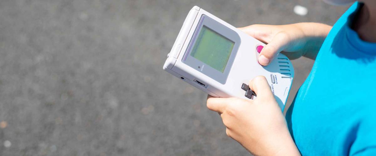 Young boy standing outside playing his video game.