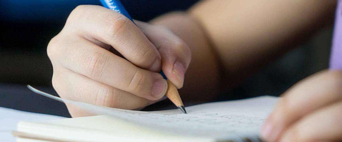 Child hand is using pencil to practice writing on a book.