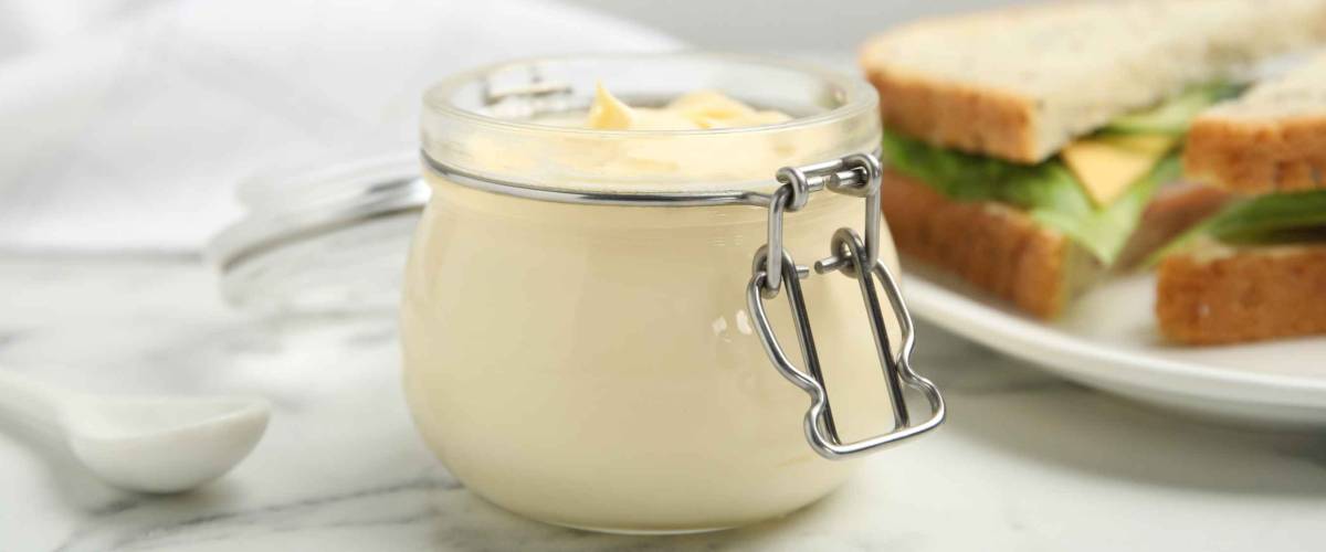 Jar of delicious mayonnaise near fresh sandwiches on white marble table