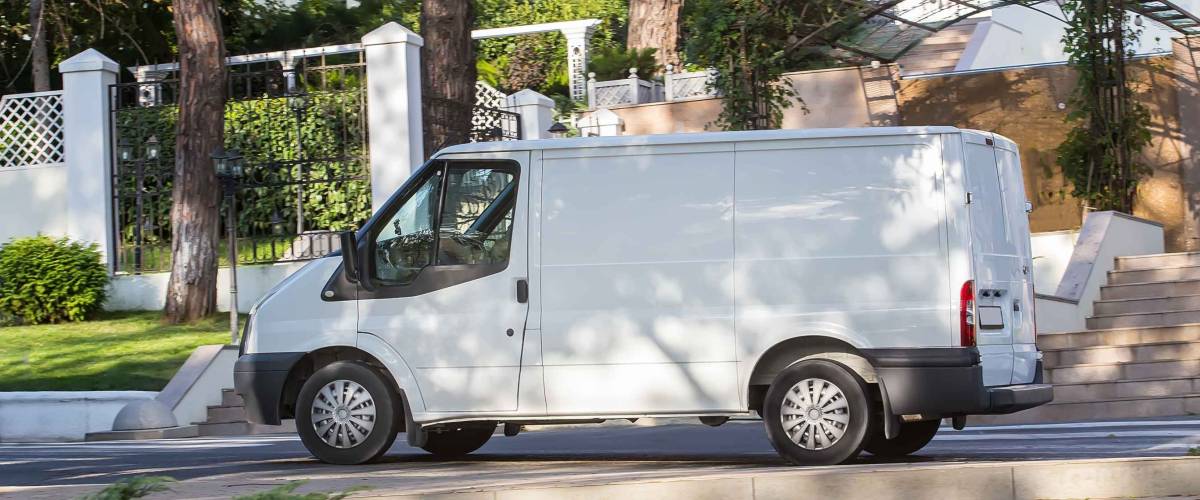 White van is parked in shade of trees on pavement