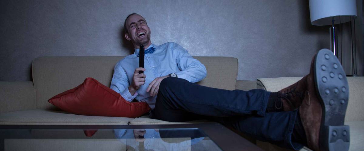 young man in a blue shirt and bow tie watching TV laughing
