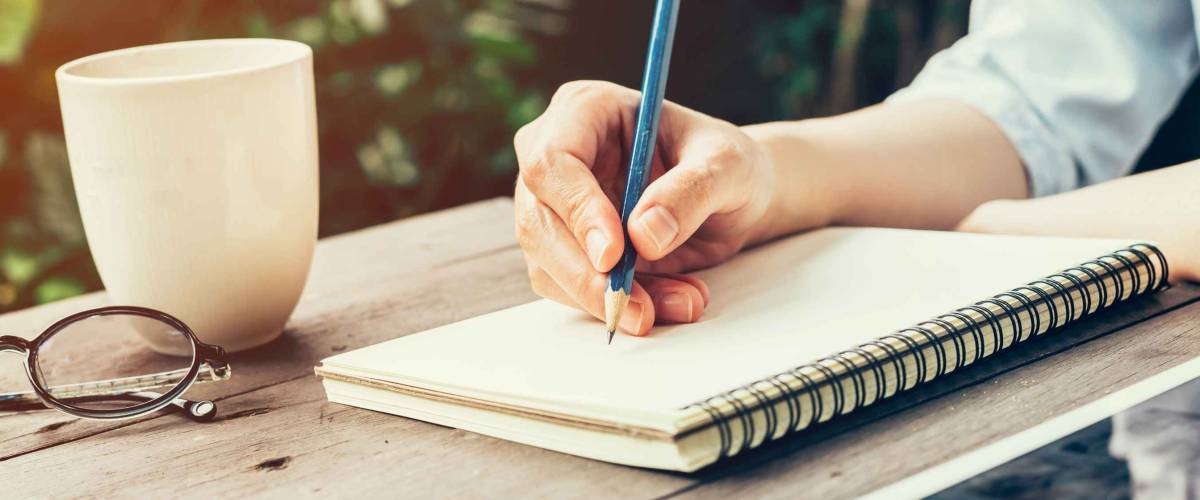 Woman hand with pencil writing on notebook at coffee shop.