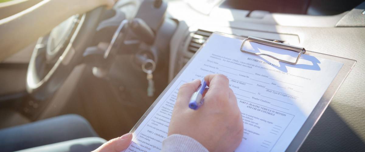 Examiner filling in driver's license road test form sitting with her student inside a car
