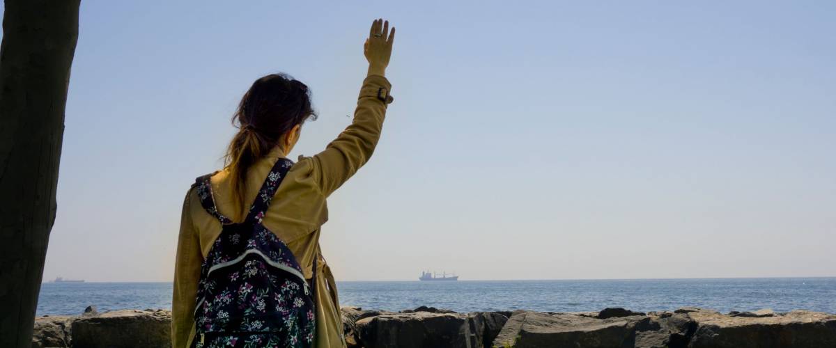 Sad woman or girl standing alone on the seaside and waving her hand to distant ship and horizon with feeling lonely.