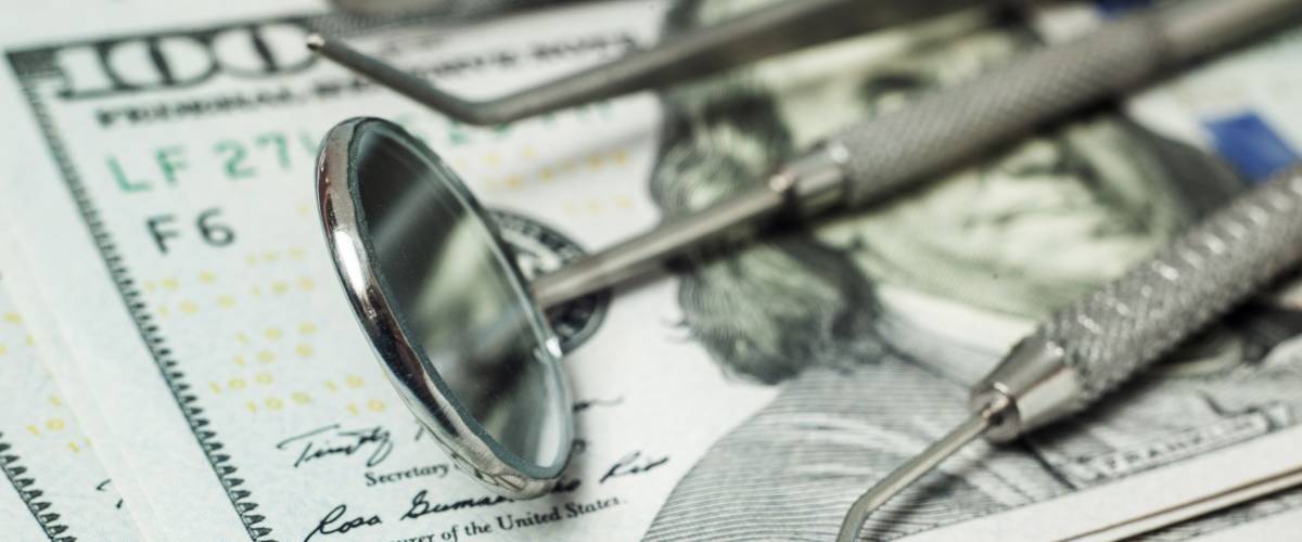 Dental tools mirror, tweezers and a hook on a stack of cash dollar bills. Concept expensive dentistry or dental insurance