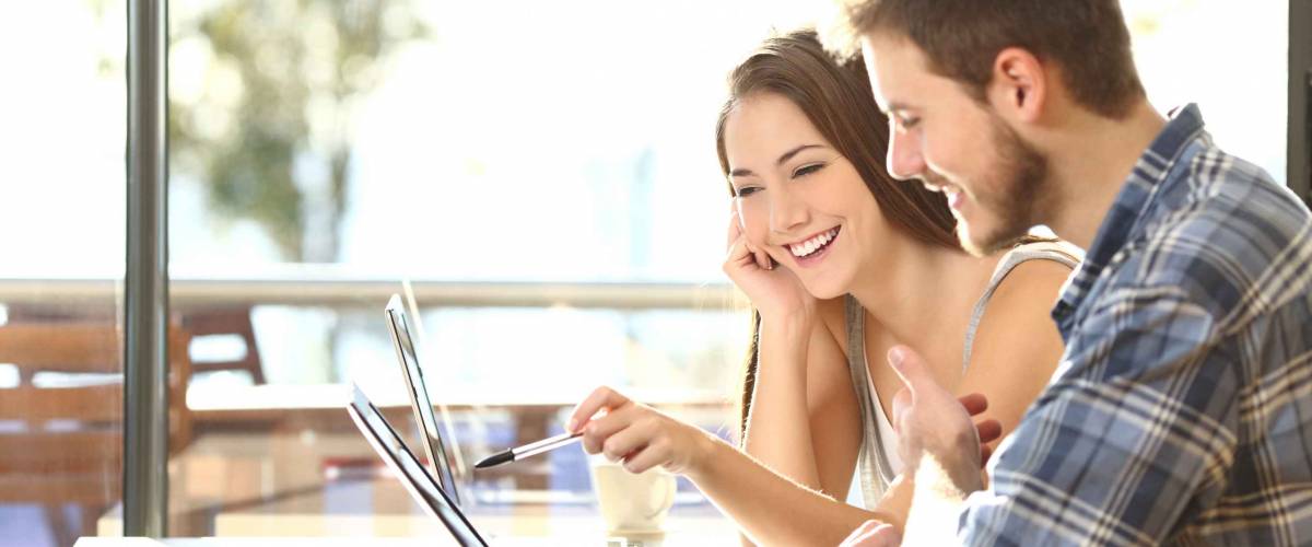 Side view of two young adult students studying and talking about lessons comparing together laptop information in a coffee shop