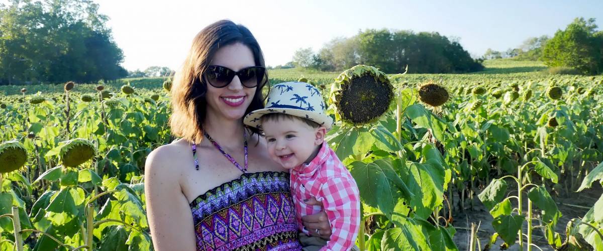 Lawrence, Kansas / United States - September 26 2015: Mom in pink printed sundress holding adorable chubby cheeked happy toddler boy in Kansas sunflower field.