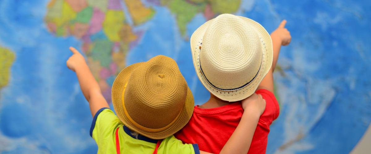 Two children who are siblings point at a world map