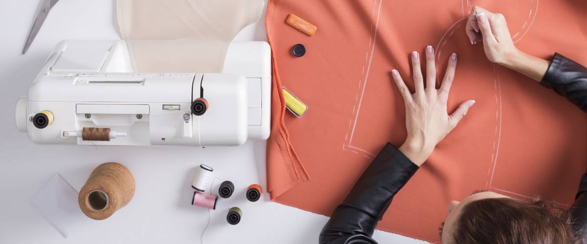 Top view of a girl making a pattern on a red piece of material. Fashion design conceptual.