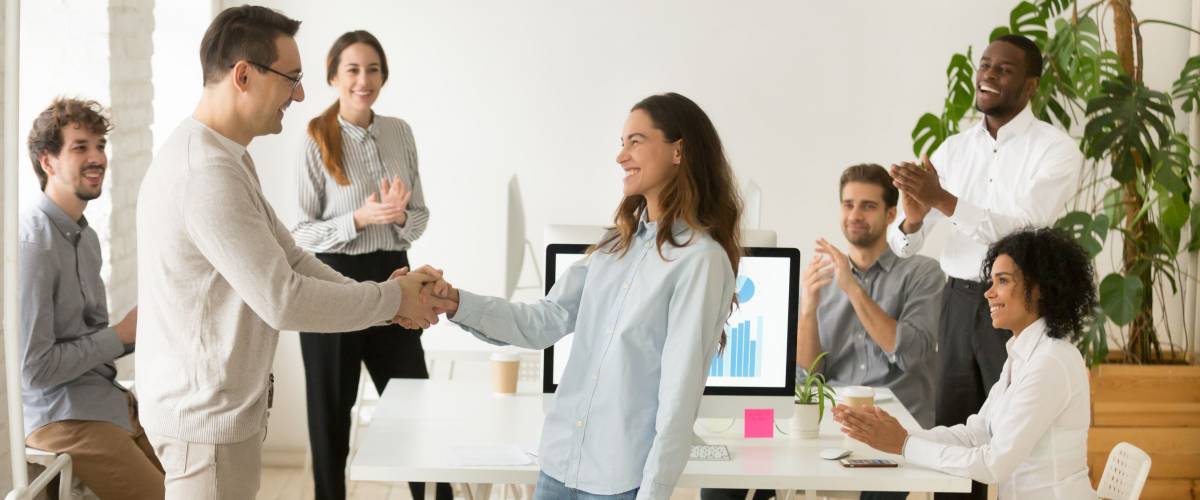 Boss shaking hand of young shy woman congratulating successful employee with promotion, hiring intern