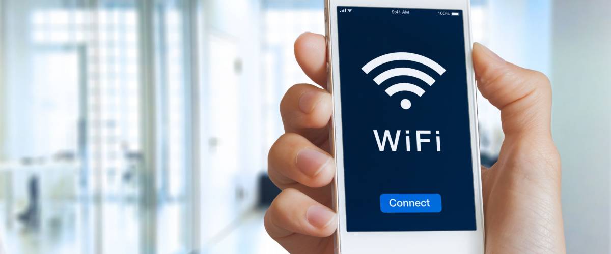 Close-up of hand holding smartphone with WiFi symbol and connect button on the screen to access public wireless internet, blurred building interior