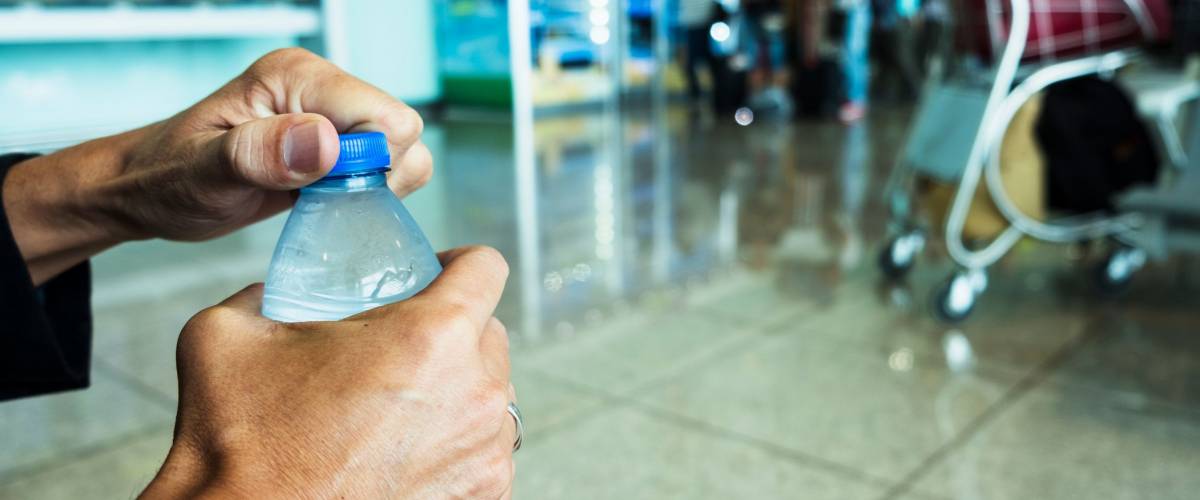 a man's hands opening a water bottle at an airport