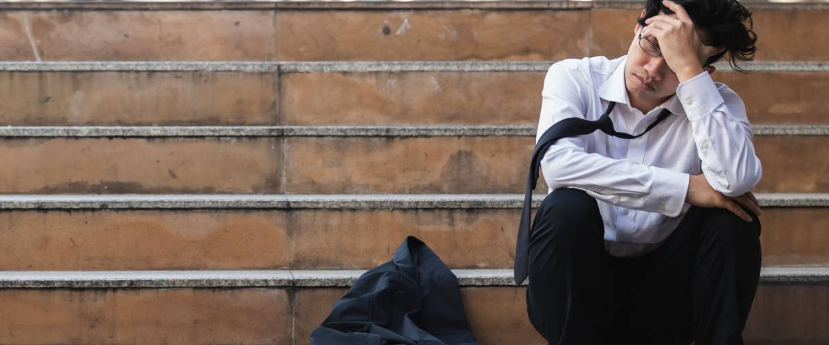 Unemployed stressed young Asian business man in suit covering face with hands. Failure and layoff concept.