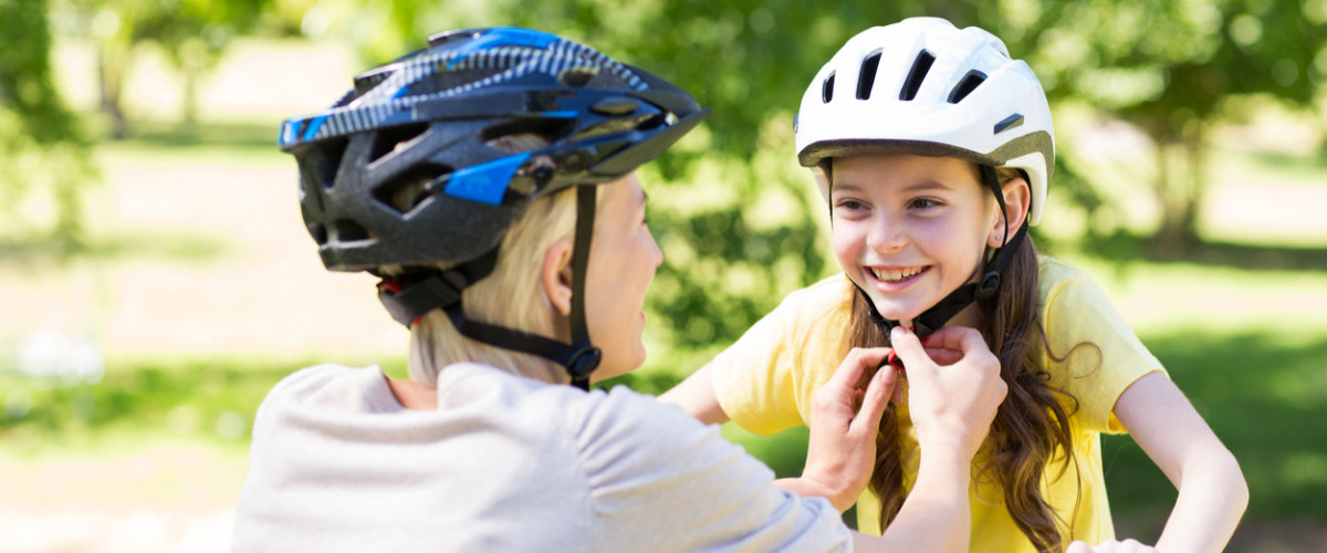 Mother attaching her daughters cycling helmet on a sunny day