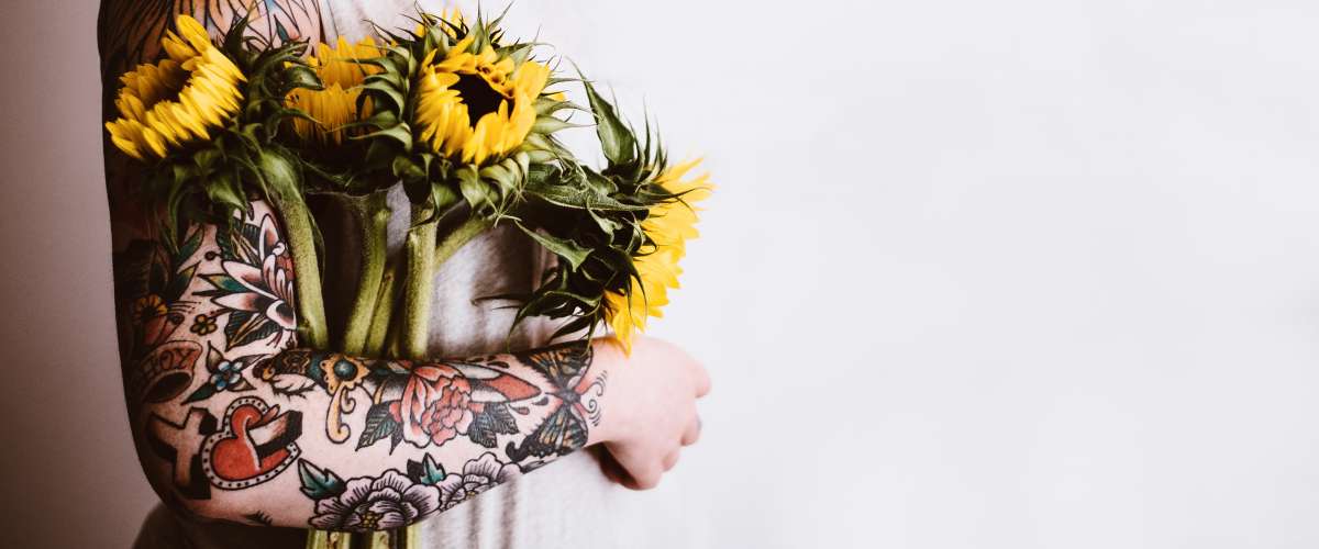 Woman with a tattooed arm holding yellow flowers