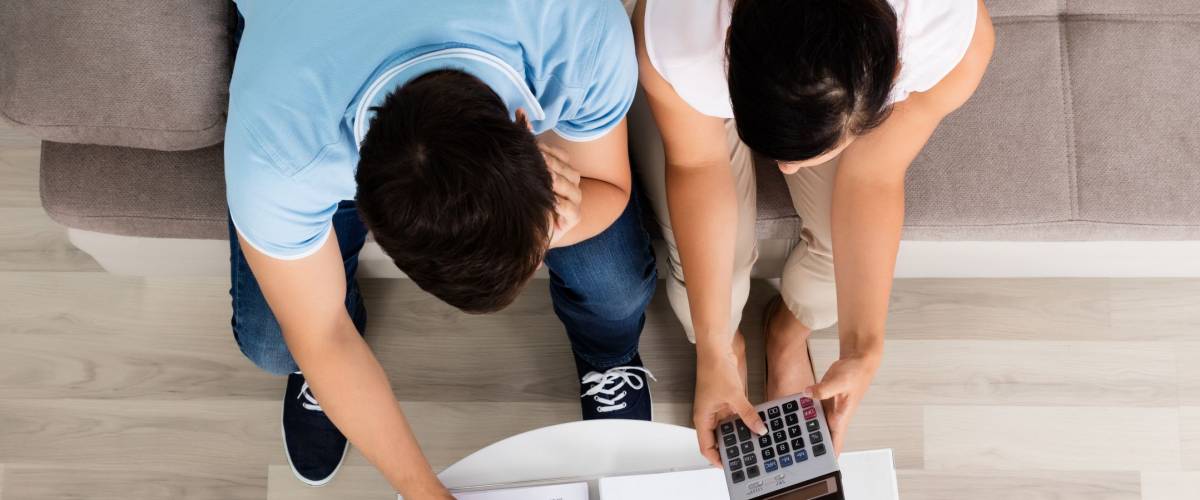 High Angle View Of Young Couple Sitting On Sofa Calculating Budget At Home