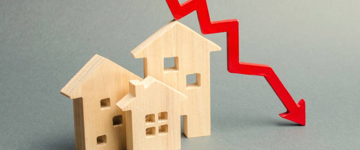 Miniature wooden houses and a red arrow down. Lower mortgage interest rates.