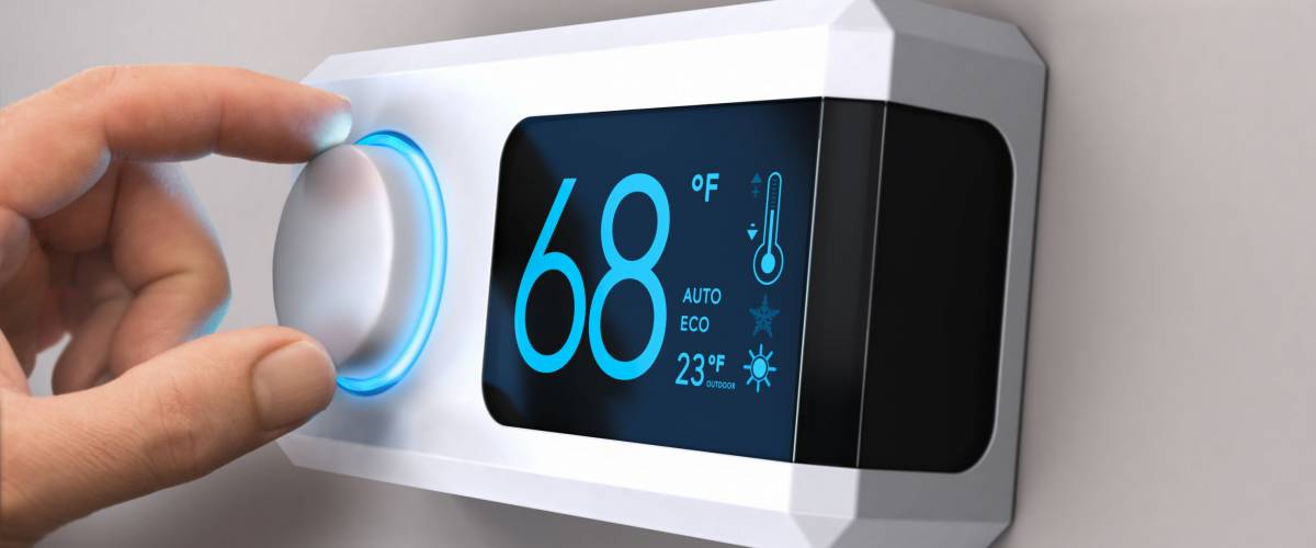 Hand turning a home thermostat knob to set temperature on energy saving mode.