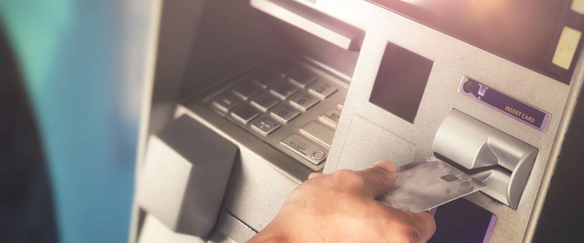 Man’s hand inserting ATM credit card into bank machine to transfer money or withdraw